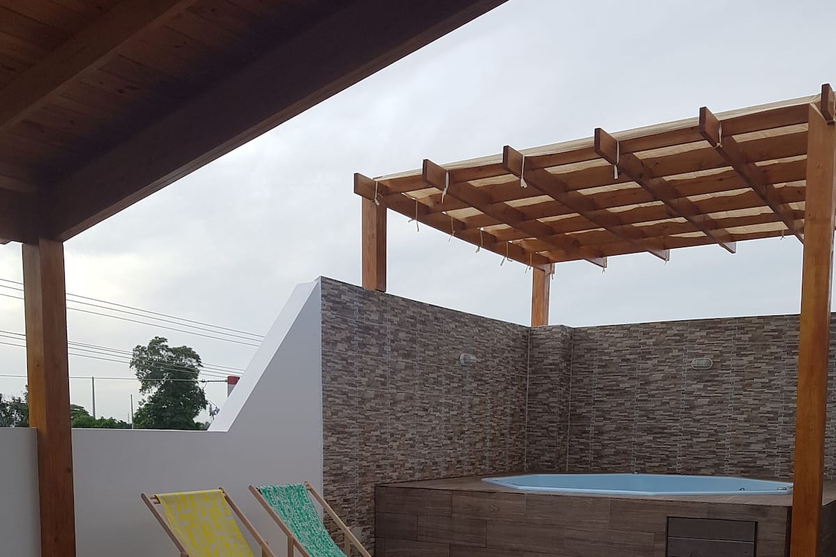 A covered outdoor area with a wooden pergola, a stone wall, and a hot tub.