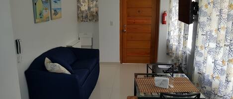 Un salón con un sofá azul oscuro, una mesa de vidrio con camino de mesa a cuadros, y una puerta de madera.
