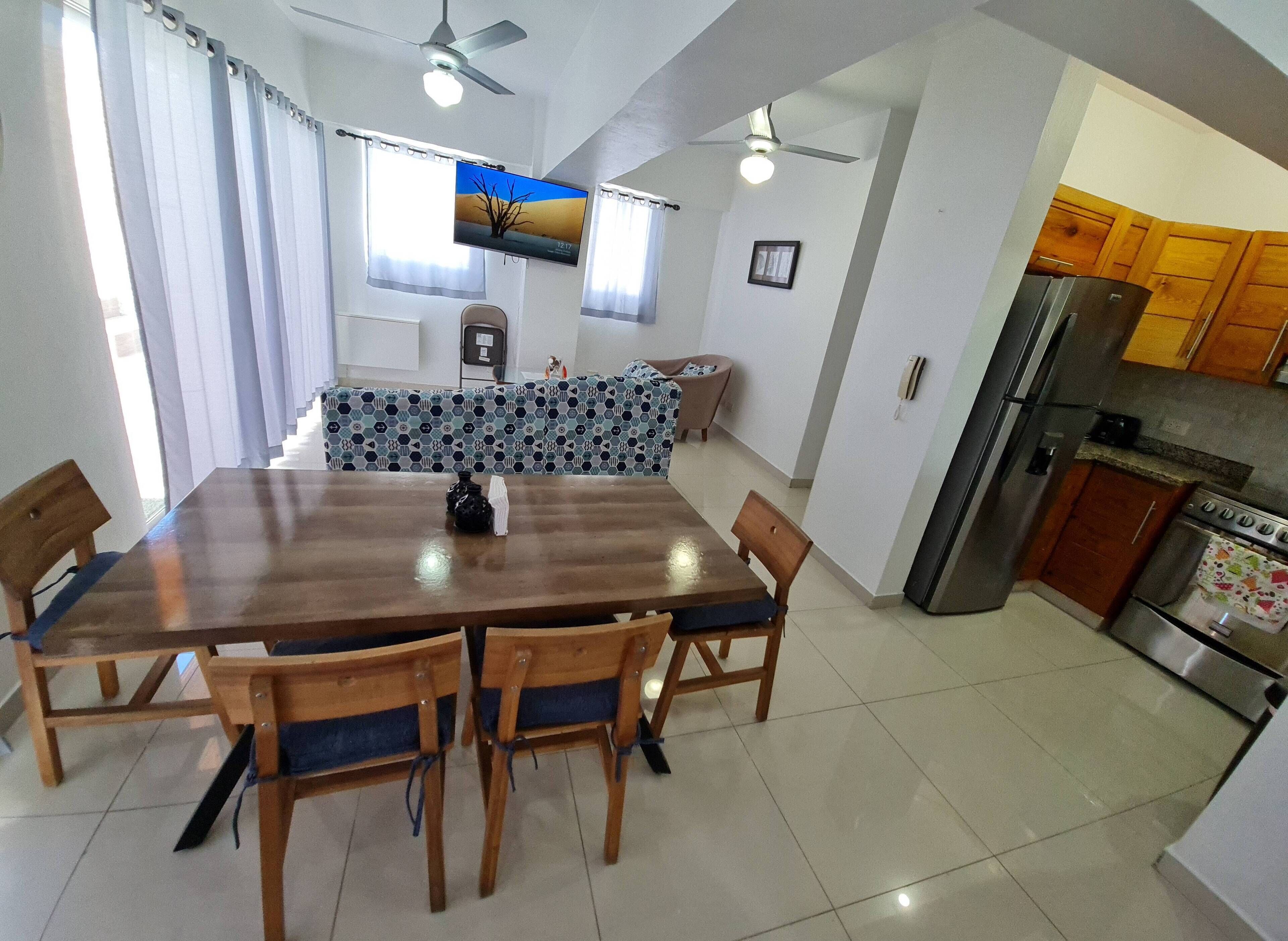 A dining area with a wooden table and chairs, a kitchen with wooden cabinets and appliances, and a ceiling fan.