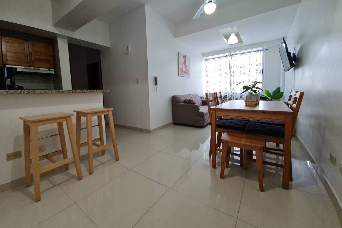 A modern kitchen with a built-in oven and microwave, a dining area with a wooden table and chairs, a ceiling fan, and a window with curtains.