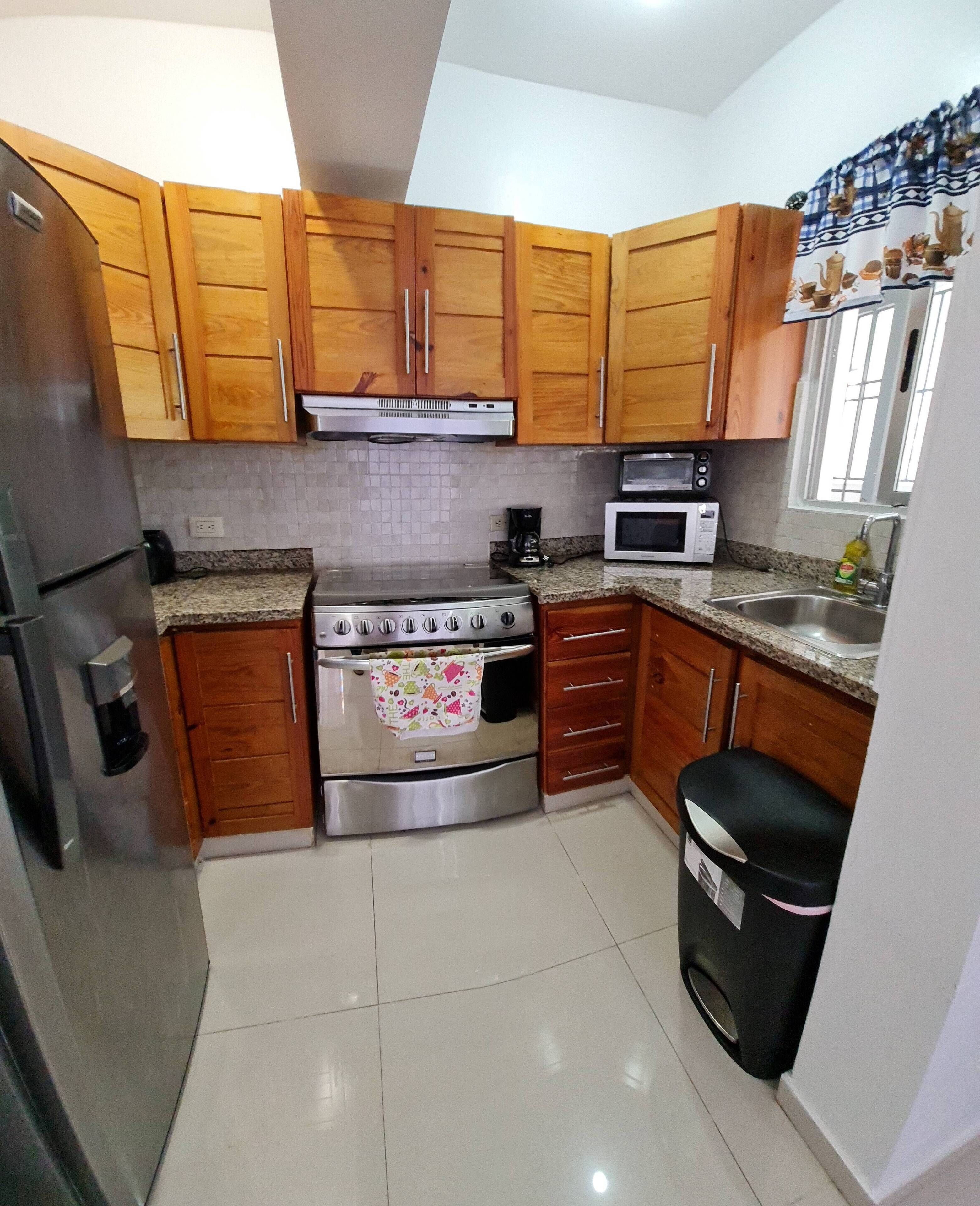 Una cocina con armarios de madera, estufa de acero inoxidable, microondas y pileta.