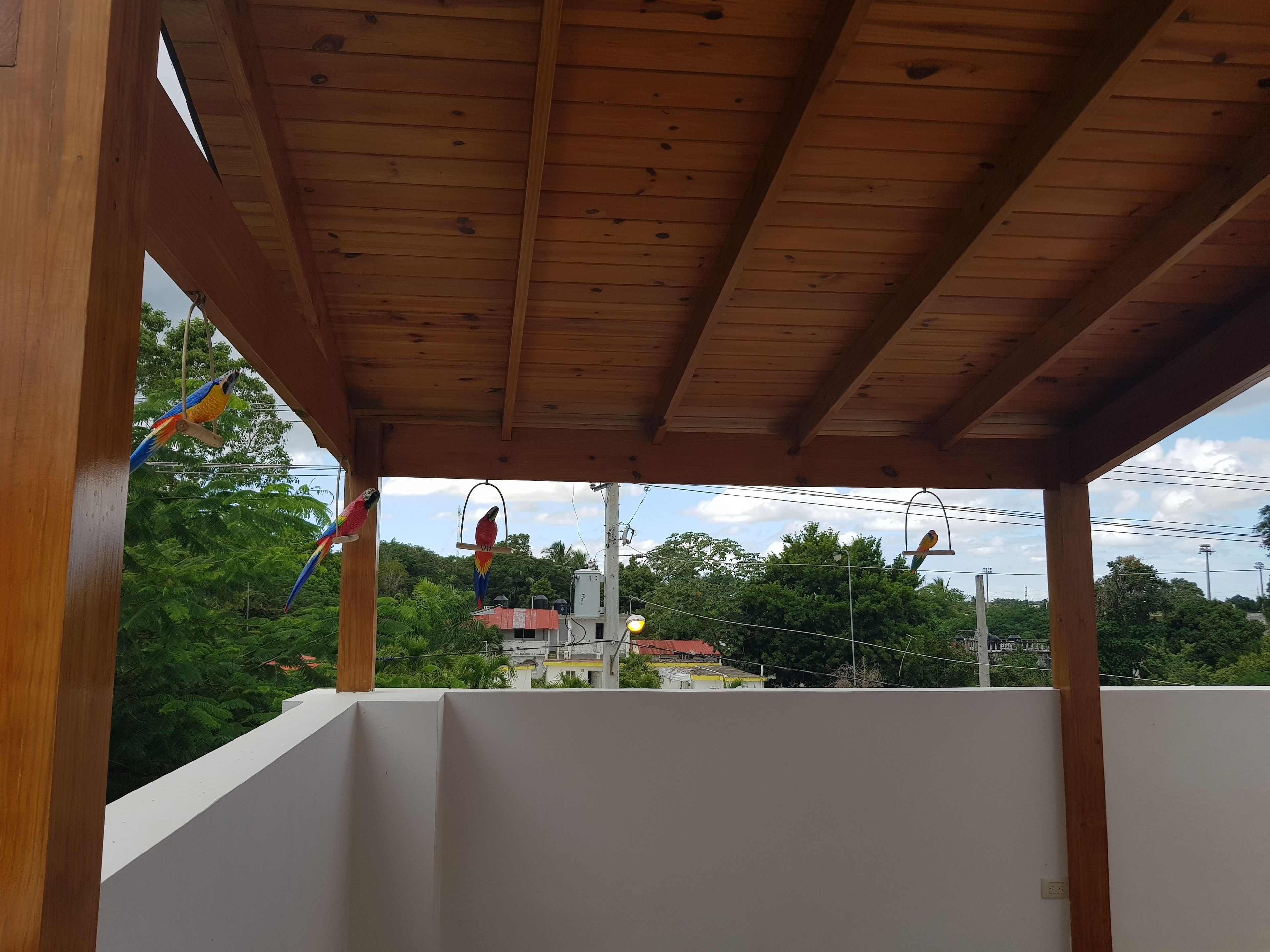 A covered outdoor area with wooden beams and a white wall.