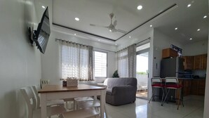 A modern kitchen with a refrigerator, microwave, and wooden cabinets. There is a dining area with a table and chairs, and a gray sofa. - KSL Residence (Boca Chica)
