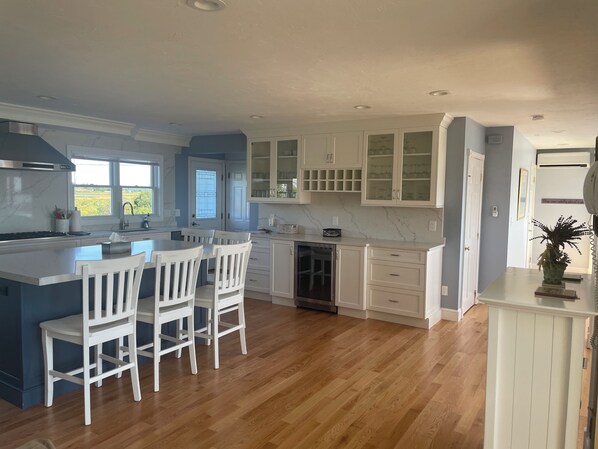 A kitchen with a central island, white cabinetry, and a view of the outdoors. - Ocean Views From Every Room, Beach 30 Seconds Away! (West Hyannisport)