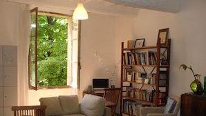 Una sala de estar acogedora con una mesa de comedor de madera, un sofá, una estantería y un televisor.