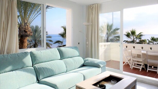 Un sofá azul claro en una habitación con ventanas amplias que ofrecen vistas a palmeras y al mar.