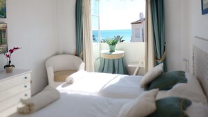 Habitación de hotel con cama, una silla, una mesita con una planta y vistas al mar.