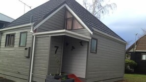Una casa pequeña de un solo piso con fachada gris, puerta principal roja y un pequeño porche con escalones.