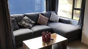 Una sala de estar moderna con un sofá seccional, una mesa de centro de madera y un ventanal con persianas.