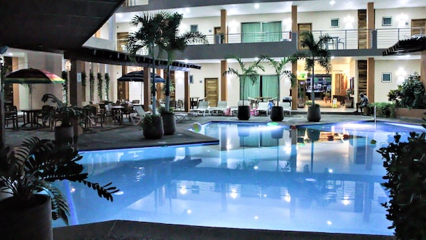 Un hotel de varios niveles con una piscina central, asientos al aire libre y plantas en macetas.