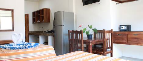 A hotel room with a bed, a desk, a refrigerator, a television, and a potted plant.