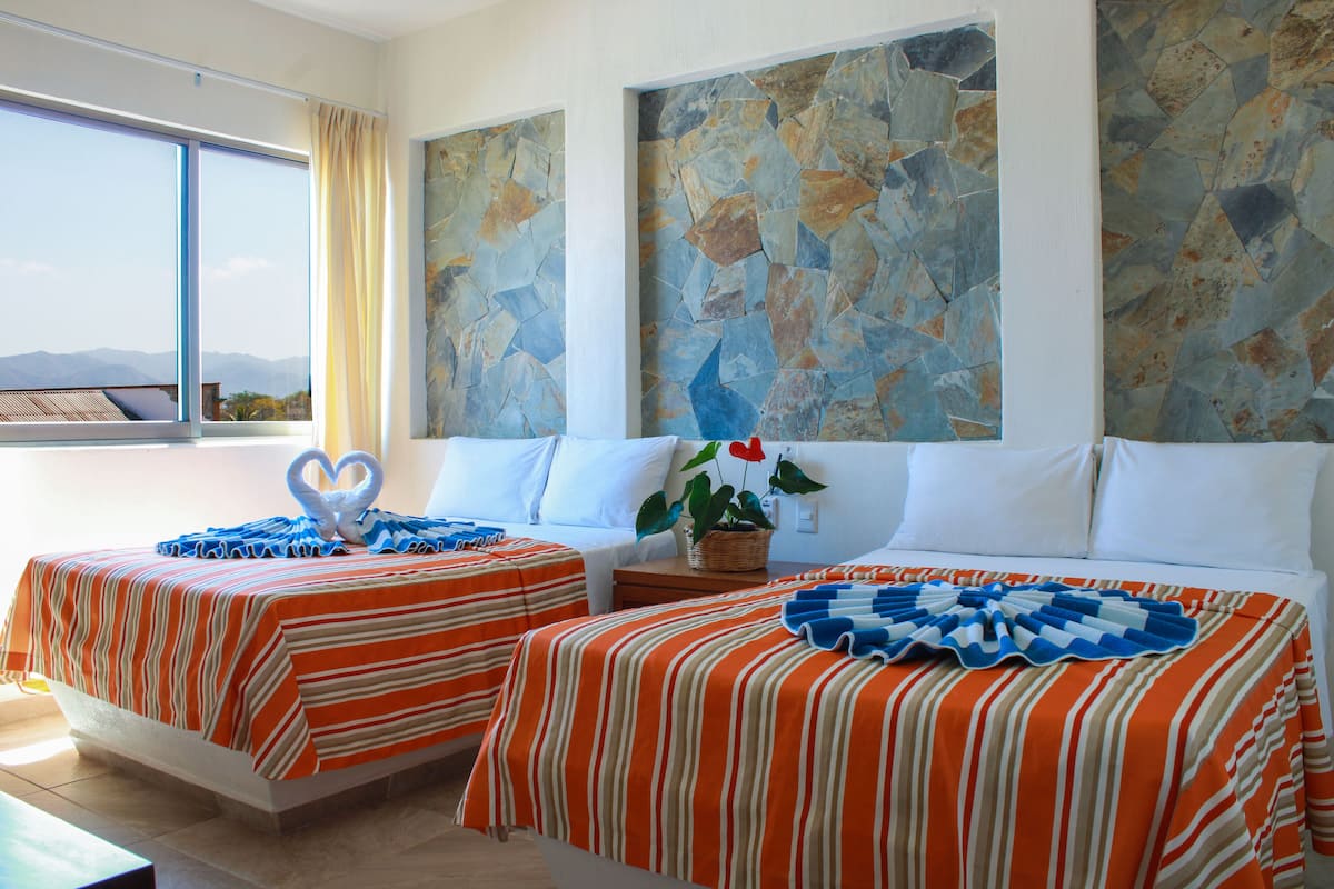 A hotel room with two beds, large windows, and a stone wall.