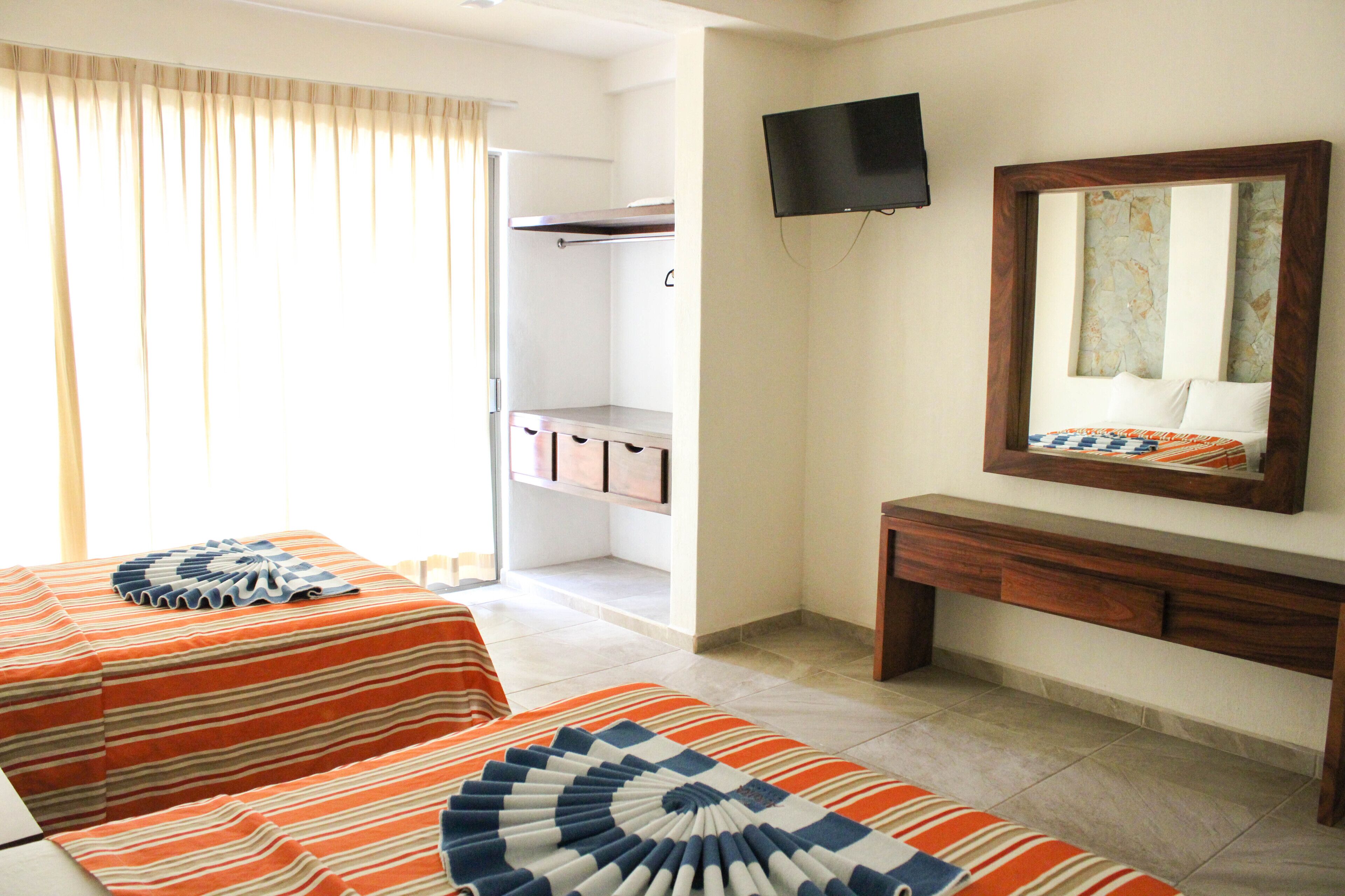 Habitación de hotel con dos camas, televisión, espejo y armario.