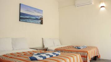 A hotel room with two beds, each with striped bedding and pillows, a painting of a beach scene, and an air conditioning unit on the wall.