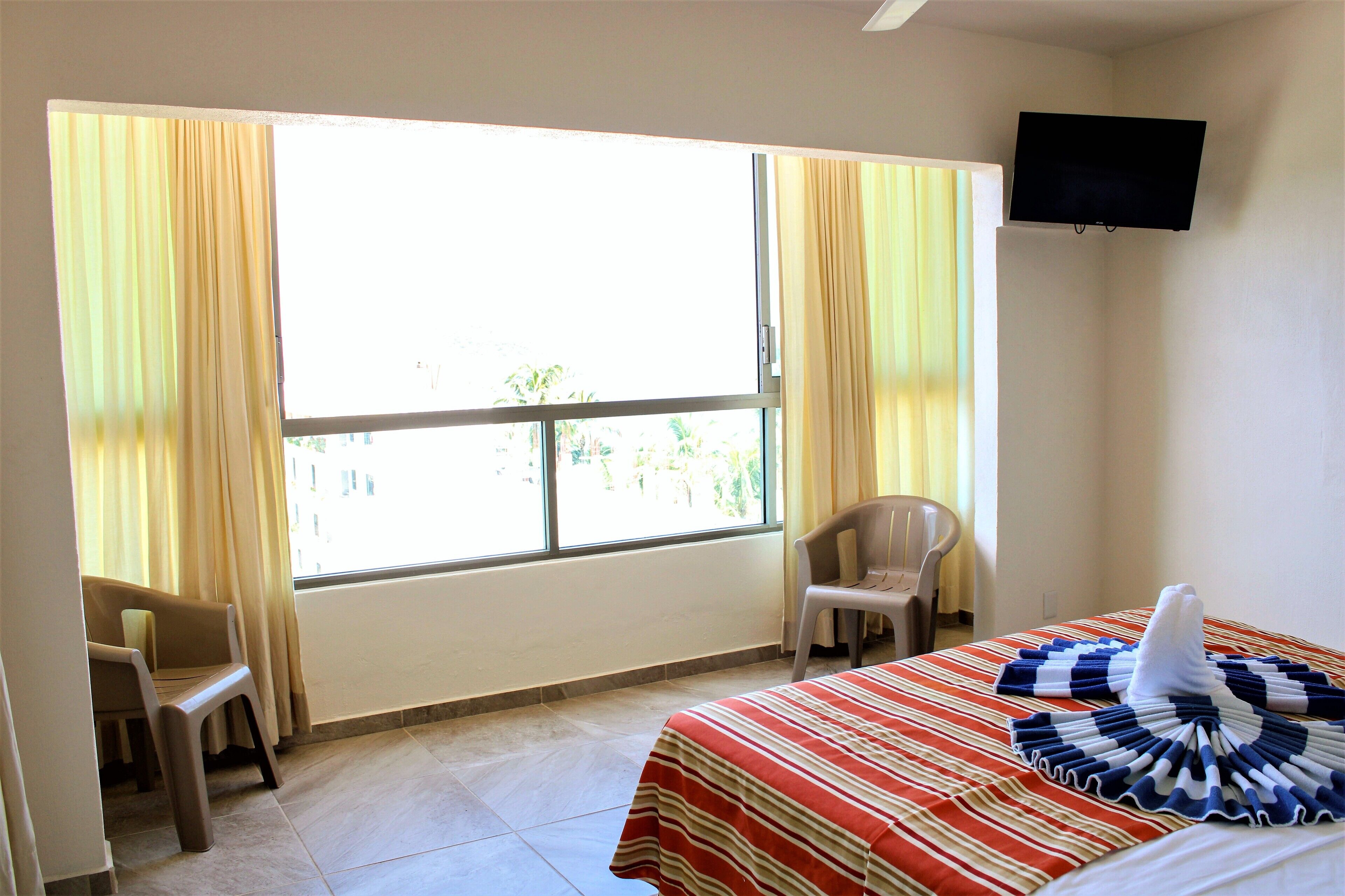 A hotel room with a bed, a chair, a television, and a window with curtains.