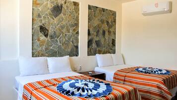 Quarto de hotel com duas camas, cada uma com roupa de cama listrada e almofada decorativa azul e branca. Duas grandes peças de arte em pedra adornam a parede sobre as camas.