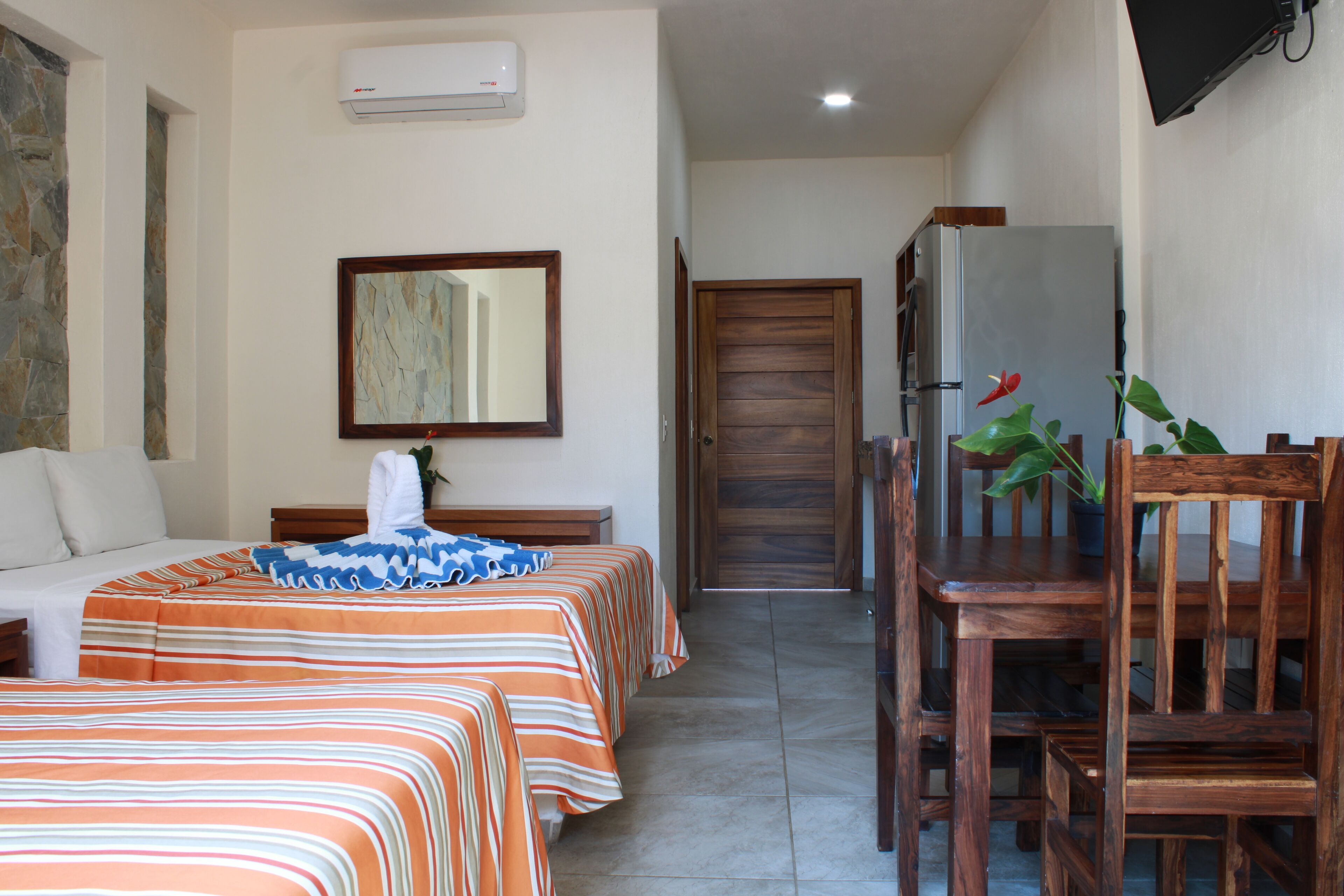 Una habitación de hotel con dos camas, una mesa de comedor de madera, un refrigerador y una planta en maceta.