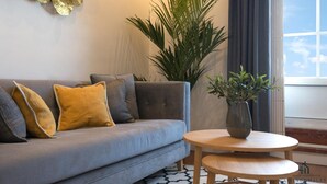 A modern living room with a grey sofa, yellow and grey cushions, a round wooden table, and a large potted plant. - Atico MarinaLiving4malaga (Málaga)