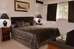 Een slaapkamer met een groot bed, twee nachtkastjes met lampen, een lijst met een foto aan de muur en een raam met gordijnen.