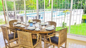 A dining area with wicker chairs and a round table set for six, overlooking a pool and garden. - VILLA PATIENTLY WAITING IS A STUNNING NORTH COAST JAMAICAN GEM A DIAMOND RENTAL (Ocho Rios)