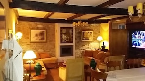 Ein gemütliches Wohnzimmer mit Steinsäulen, Holzbalken, einem Kamin und einem Fernseher.