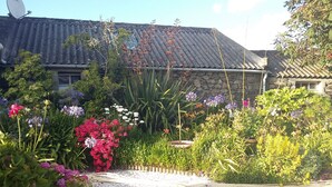 Ein Garten mit verschiedenen blühenden Pflanzen und einem Gebäude mit einem Ziegeldach.