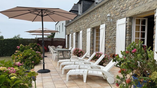 Ein Steinhaus mit einer Terrasse, die Gartenmöbel, einen Tisch und Kübelpflanzen zeigt.