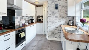 Eine moderne Küche mit weißen Schränken, einer Holz Arbeitsplatte, einem eingebauten Ofen, einer Mikrowelle und einem Spülbecken mit Blick aus dem Fenster.