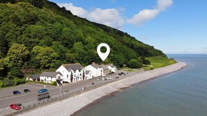 Eine Küstenstraße mit weißen Gebäuden, einem Strand und einem bewaldeten Hügel.