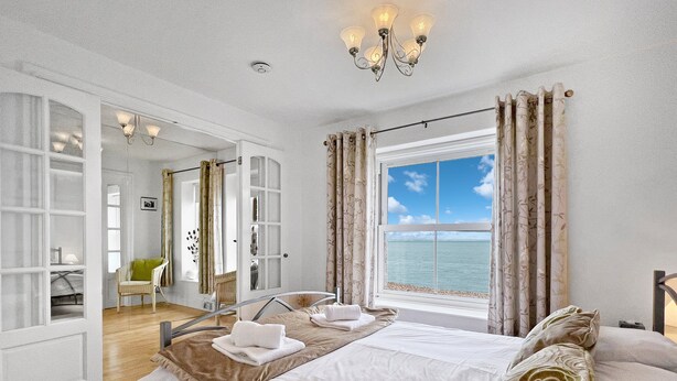 Ein Schlafzimmer mit einem großen Bett, Meerblick und einem Badezimmer mit Dusche und Stuhl.