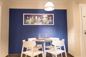 Ein Essbereich mit blauer, strukturierten Wand, einem gerahmten Blumenbild, weißen Stühlen und einem Tisch, der mit Weingläsern und Tellern gedeckt ist.