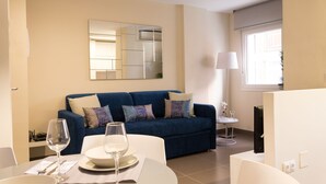 A modern living room with a blue sofa, a dining table with a glass of wine, and a large mirror on the wall.