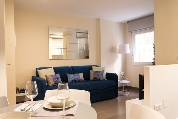 A modern living room with a blue sofa, a dining table with a glass of wine, and a large mirror on the wall.
