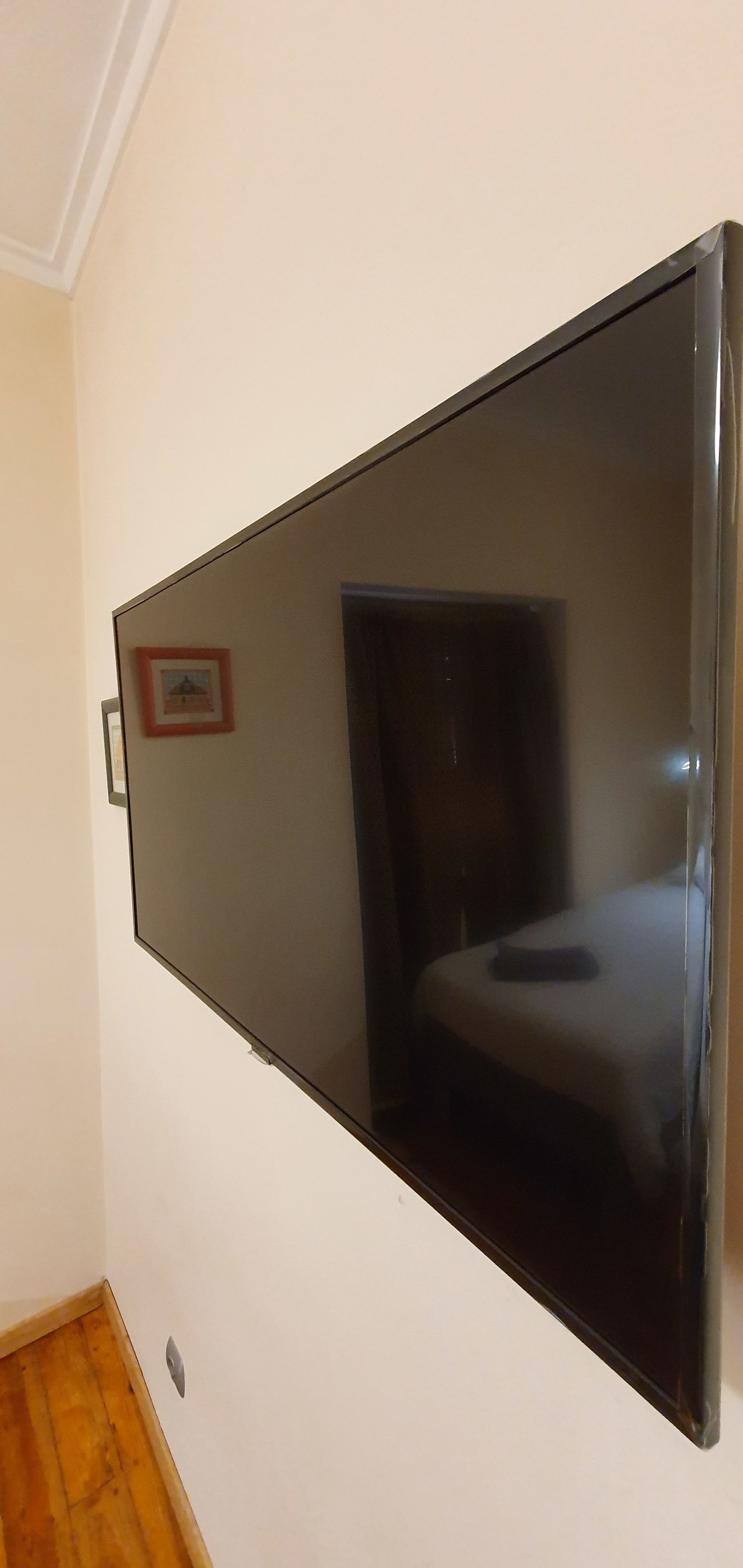 A room with a large flat-screen TV mounted on the wall, a framed picture on the wall, and a wooden floor.