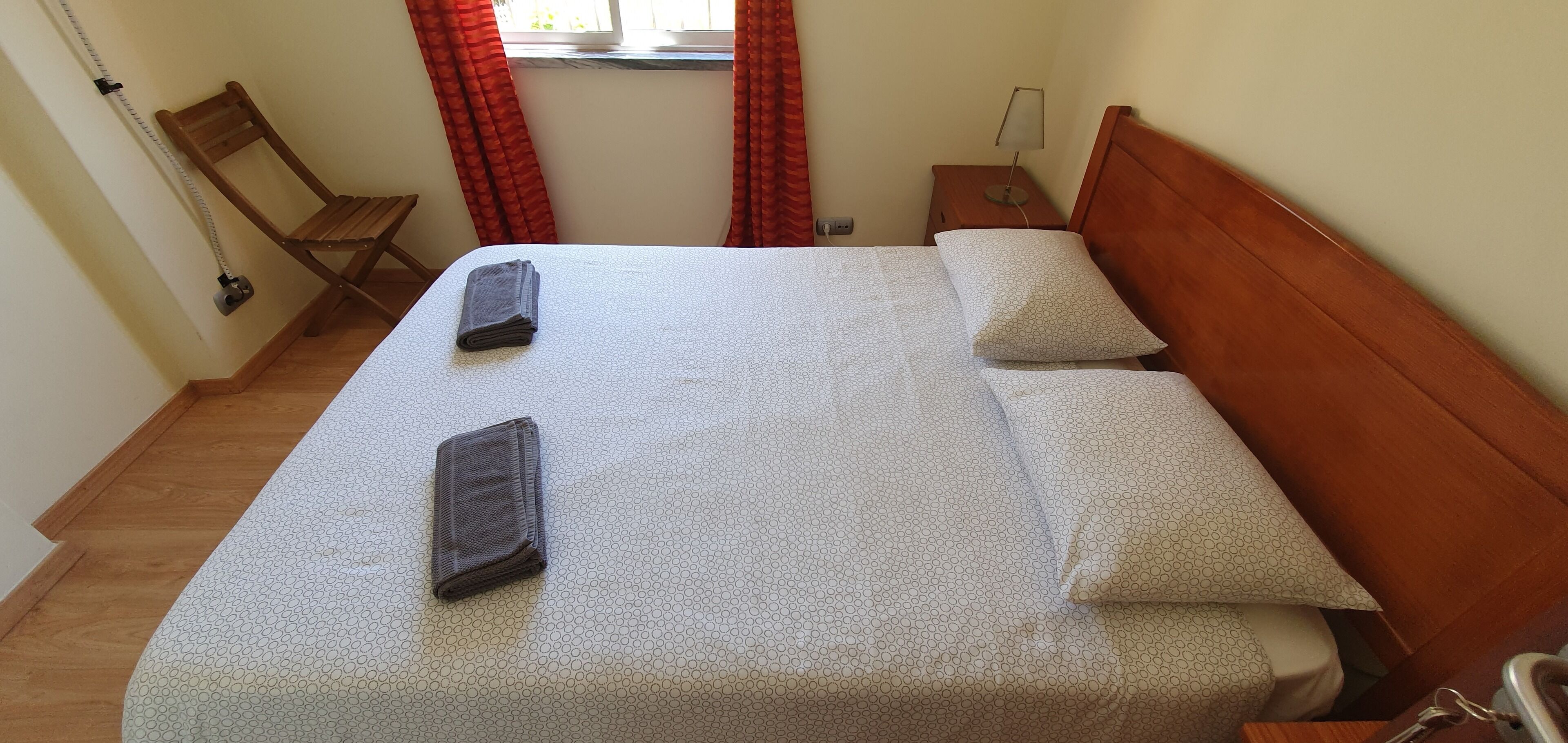 Un lit bien fait, avec un couvre-lit blanc à motifs, deux oreillers et une couverture pliée.