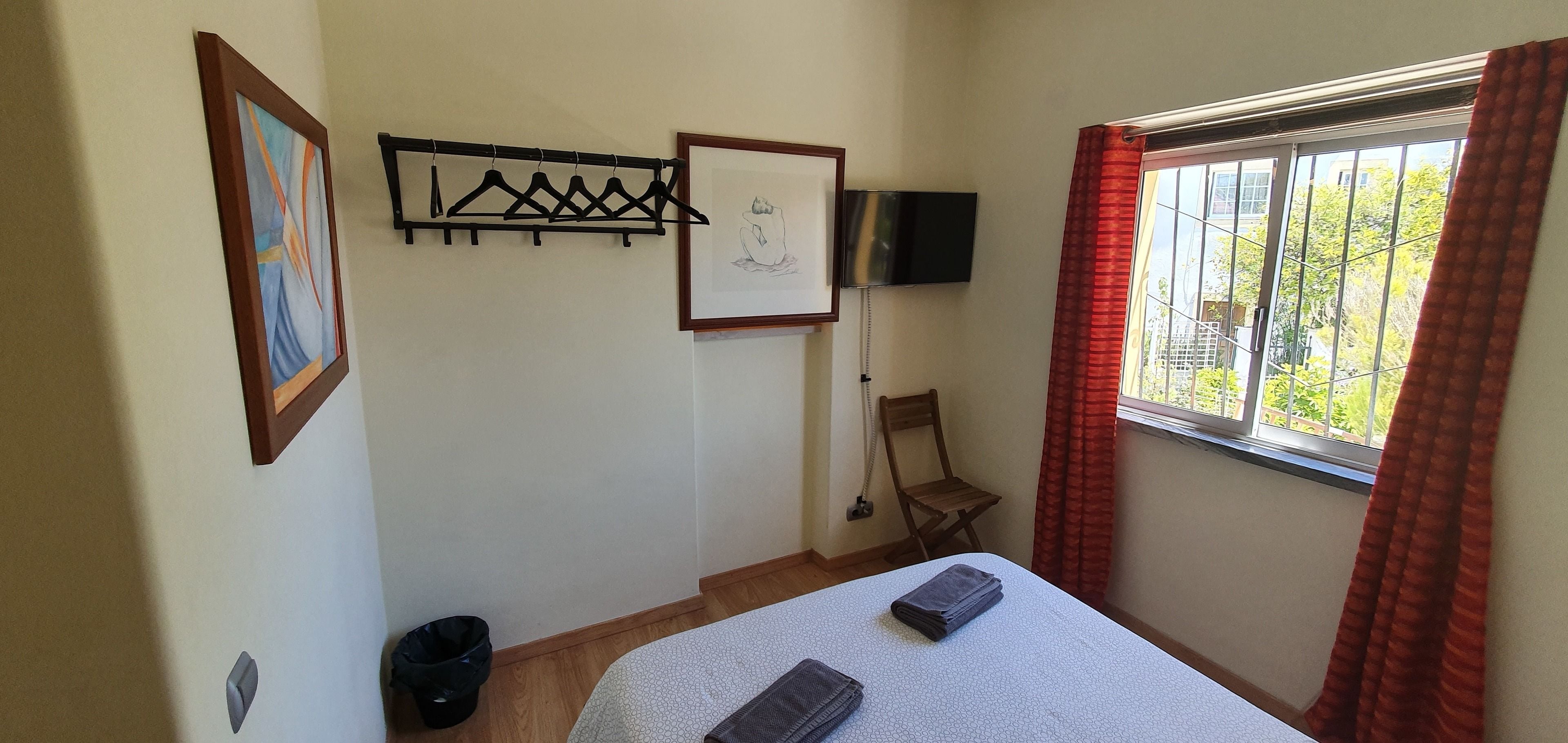 A bedroom with a bed, a TV mounted on the wall, a chair, and a window with curtains.