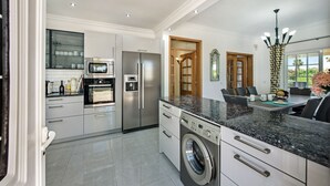 A modern kitchen with stainless steel appliances, a built-in washer, and a dining area with a table and chairs. - Luxury Gated Villa | Private Pool | Sesmarias near Carvoeiro (Carvoeiro)