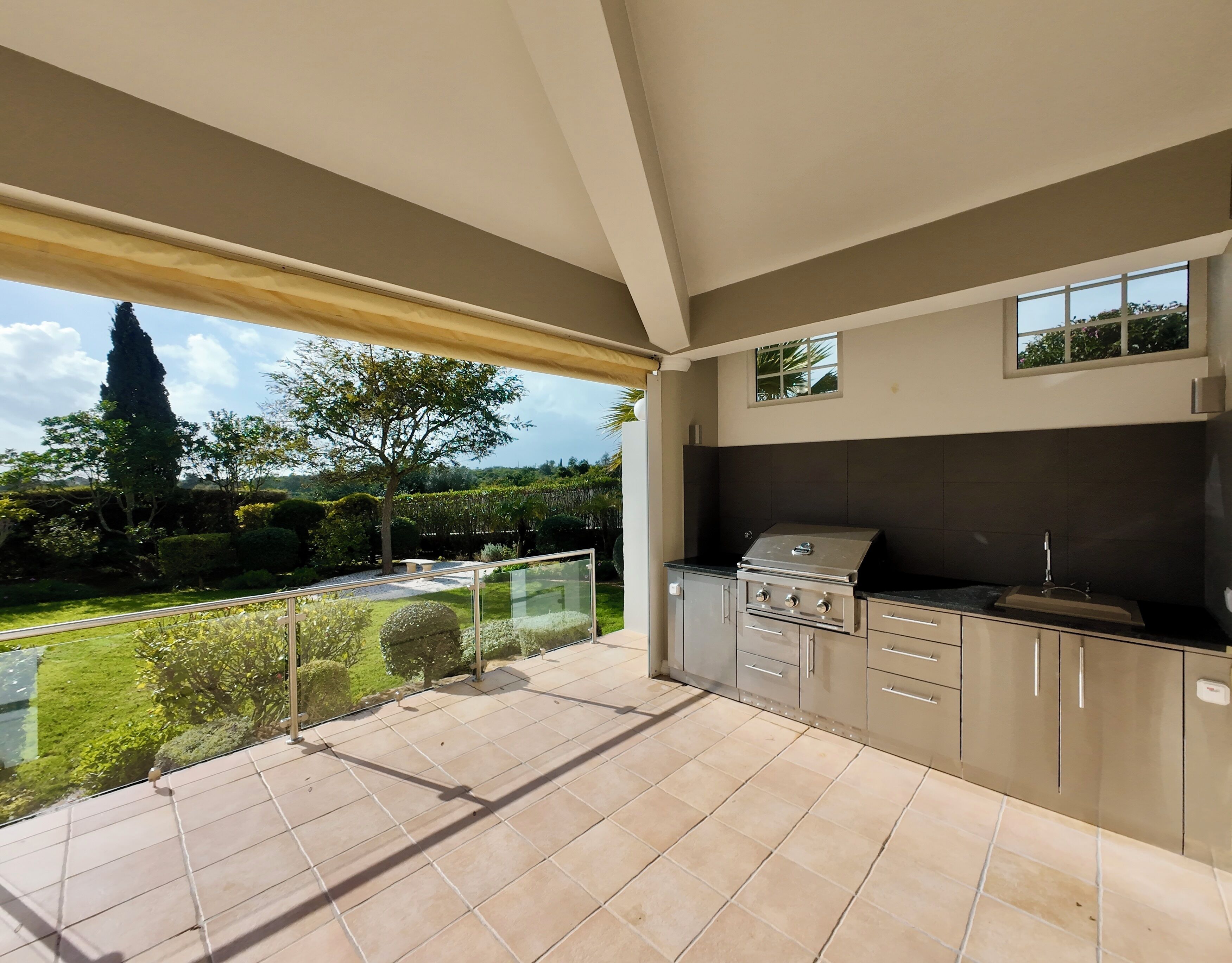 A modern kitchen with a built-in grill, large windows, and a view of a landscaped garden.