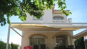 Ein überdachter Patio-Bereich mit Gartenmöbeln, ein kleines Spielhaus für Kinder und ein Gebäude mit Steinverkleidung.