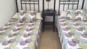 Ein Doppelzimmer mit zwei Betten, jeweils mit einem gepunkteten Bettüberwurf, einem Nachttisch mit Lampe und einem kleinen Beistelltisch.