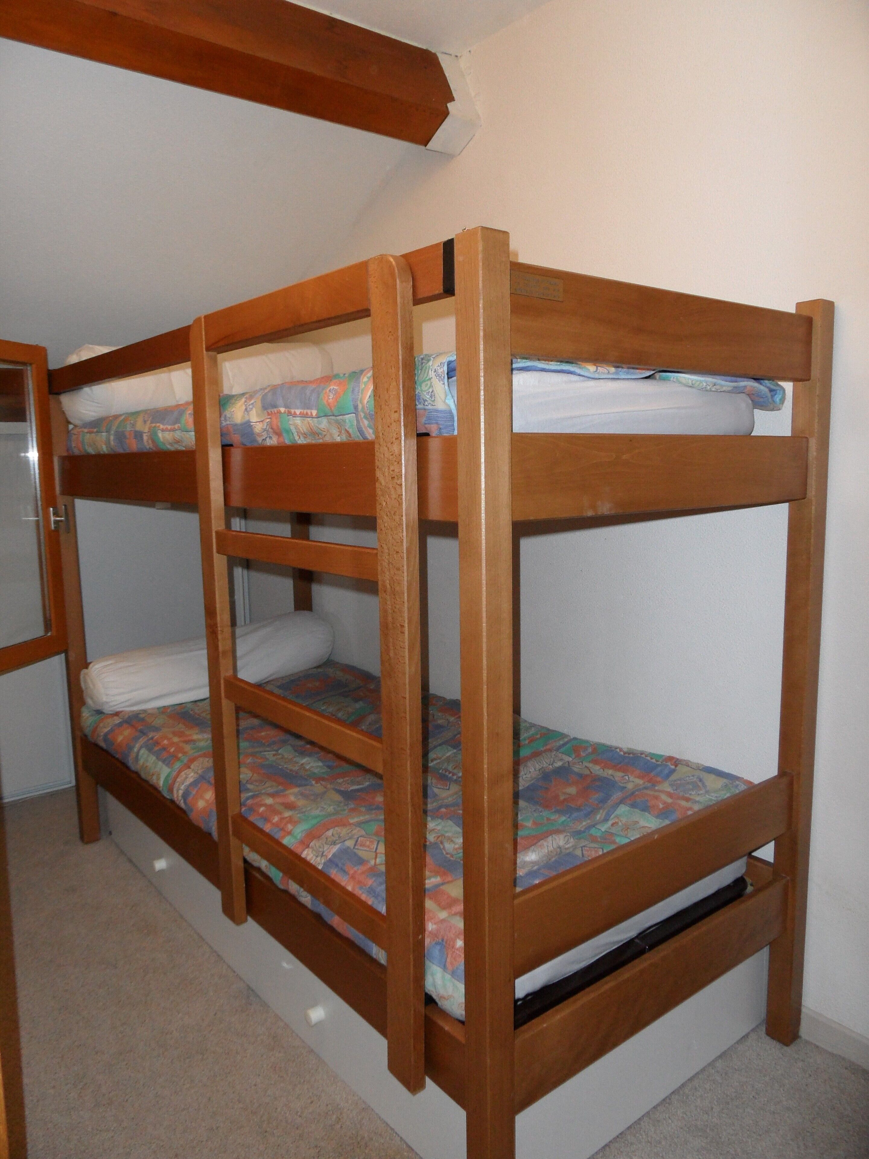 Een stapelbed met houten frame en kleurrijk beddengoed.