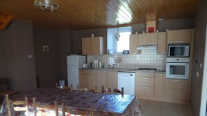 A kitchen with wooden cabinets, a microwave, an oven, a dishwasher, and a dining table with chairs. - stone house Saint Léger de Peyre (Saint-Léger-De-Peyre)