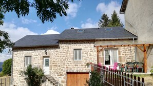 A stone house with a wooden porch, a staircase, and a fenced garden area. - stone house Saint Léger de Peyre (Saint-Léger-De-Peyre)