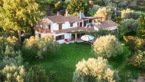 Une maison à deux étages avec un grand jardin, une terrasse dotée d’une table et de chaises, et une pergola.