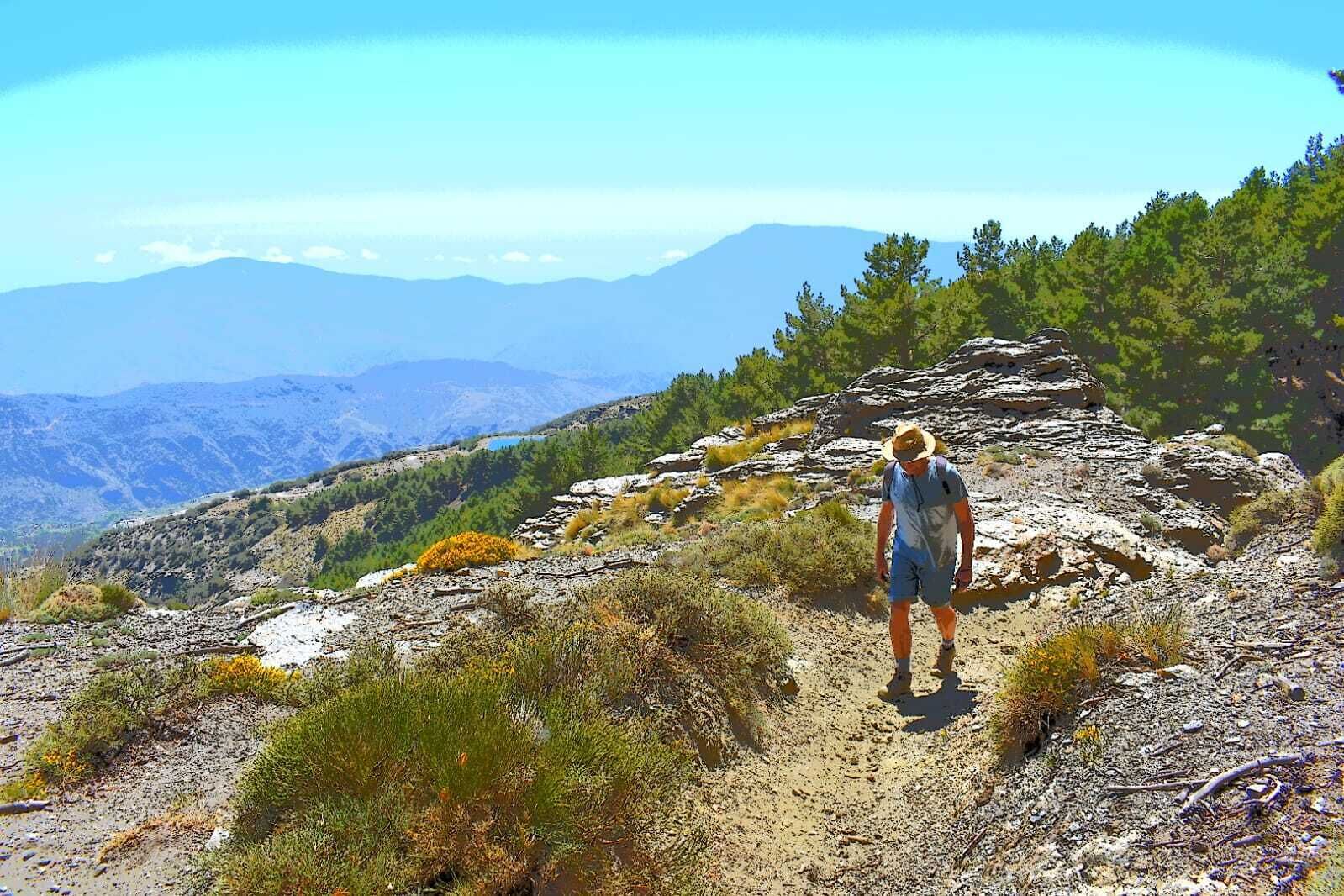 A hiker on a rocky trail with mountains in the background.