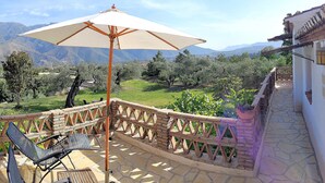 Un balcon avec une table et des chaises, un grand parasol et une vue sur un paysage montagneux.