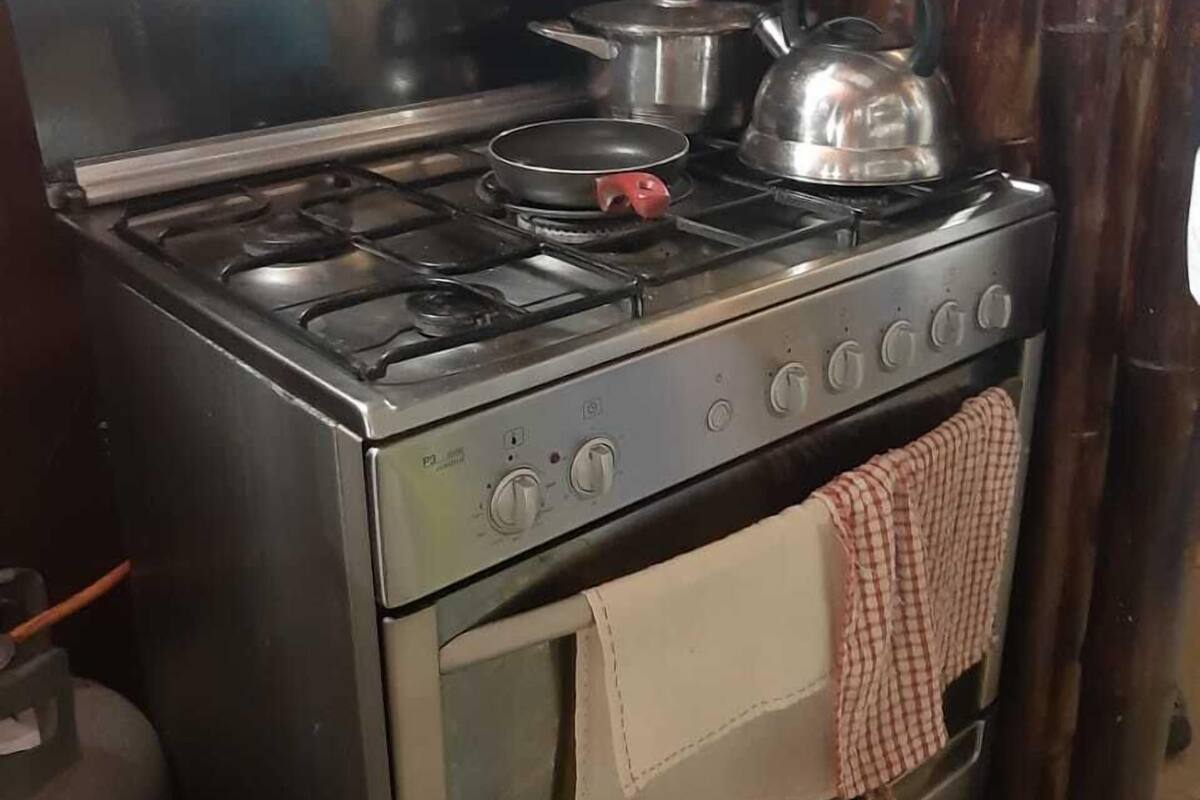 A stainless steel stove with a pot and kettle, a checkered towel, and a wooden cabinet in the background.