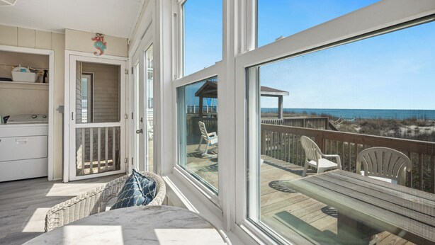 A balcony with a view of the ocean, wicker furniture, and a wooden deck. - Rhoney R&R: Oceanfront Home With Two Living Rooms (Oak Island)