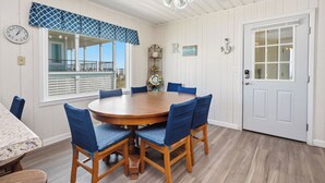A dining area with a round table, blue chairs, a ceiling fan, a clock, and a door with a window. - Rhoney R&R: Oceanfront Home With Two Living Rooms (Oak Island)
