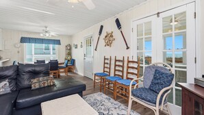 A room with a sofa, chairs, a ceiling fan, and a view through a large window. - Rhoney R&R: Oceanfront Home With Two Living Rooms (Oak Island)